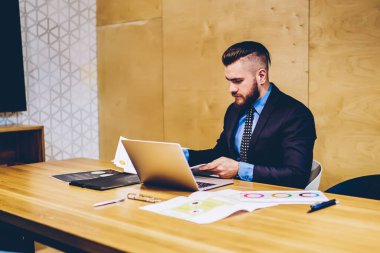Resmi giysiler içinde başarılı deneyimli bir CEO belgeleri kontrol ediyor ve kablosuz internet kullanarak dizüstü bilgisayarda çalışıyor. Modern ofiste netbook ile masaüstünde oturan düşünceli girişimci.