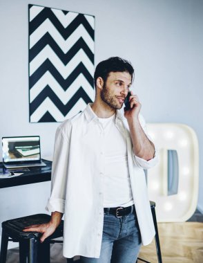 İş yerinin yanında çalışan, cep telefonuyla iş hakkında konuşan beyaz tenli olumlu bir hippi. Sıradan giyinen yakışıklı bir erkek operatörle cep telefonuyla bankacılık yapıyor.