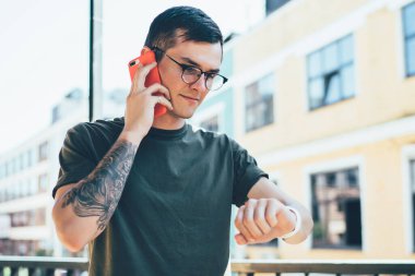 Beyaz çağdan kalma hippi adam arkadaşınla buluşmayı beklerken takılabilir akıllı saati kontrol ediyor ve detayları soruyor. Gözlüklü genç adam iletişim kurmak için dolaşım bağlantısını kullanıyor.