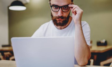 Görme koruması için gözlüklü konsantre hipster adam birlikte çalışma alanında dizüstü bilgisayarla çalışıyor. Netbook 'taki derslerden ders alan zeki erkek öğrenci.