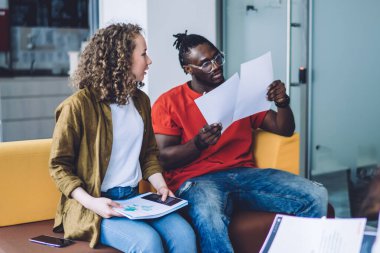 Modern çok ırklı kadınlar ve erkek modern ofiste koltukta oturuyor ve takım halinde proje planı üzerinde çalışırken gazete okuyor.