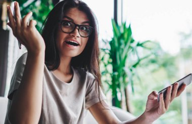 Duygusal hippi kız kameraya bakıyor ve iyi haberlerle şaşırıyor cep telefonuyla, çevrimiçi yarışmanın genç kadın kazananının portresi zaferle şok oldu.