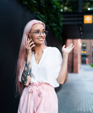 Genç, yaratıcı, uzun, parlak gül saçlı, şık yaz kıyafetleri giyen, cep telefonuyla konuşan ve gözlerini kaçıran bir kadın.