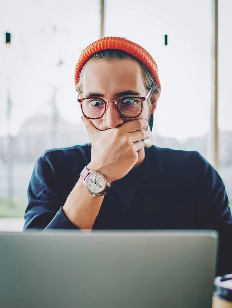 Shocked young hipster guy in spectacles amazed with 4G connection watching webinar online on netbook, surprised caucasian male shocked with received email about web store sales on laptop computer