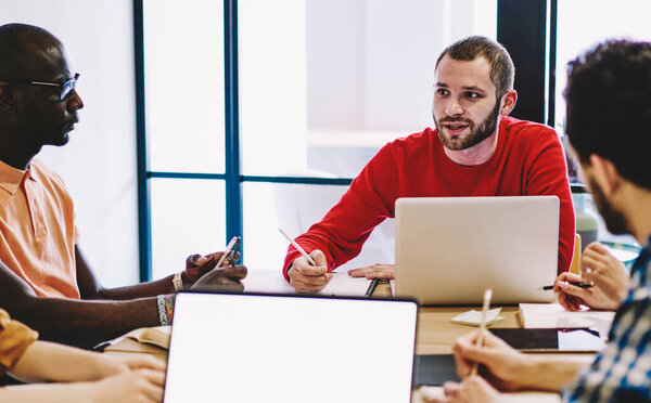 Leader of multiracial working team having meeting with crew discussing plans and strategy in modern office, owner of business communication with company staff using netbook during conversation