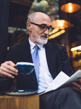 Sakallı, kahve fincanı bardaklı ve takım elbiseli, camlara gazete okuyan yakışıklı adam.