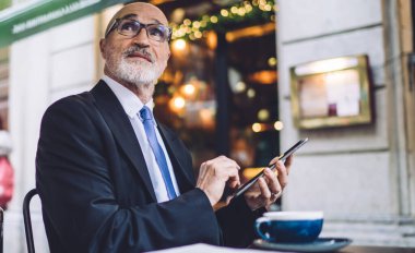 Zarif kıdemli işadamı elinde kahve fincanıyla masada oturuyor ve sokakta bulanık geçmişine bakarken akıllı telefondan mesaj atıyor.