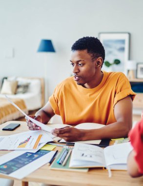 Ciddi Afrikalı Amerikalı hippi, oda kirası için fatura okuyor. Dairede kız arkadaşıyla masada oturuyor. Koyu tenli erkek ve kadın hipsterler birlikte bilgi analiz ediyorlar.