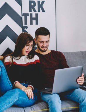 Genç evlilik rahat bir kanepede dinleniyor ve modern dizüstü bilgisayarda sosyal ağda komik videolar izliyor birlikte boş zaman geçiriyorlar, aşık çift internet üzerinden alışveriş yapıyor kablosuz internet kullanarak