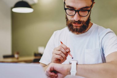 Akıllı ekranda ayarlar yaparken dizüstü bilgisayarda çalışan yetenekli erkek serbest yazar. Konsantre hipster adam, çağdaş kol saatinde Wi-Fi kullanarak GPS 'i takip ediyor.