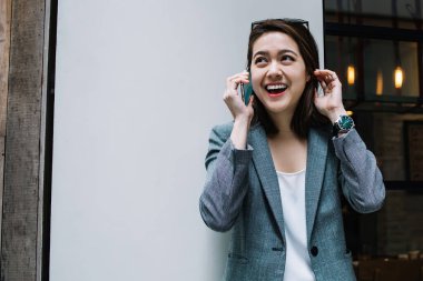 Güzel, neşeli, resmi giyinmiş genç bir kadın akıllı telefonuyla gülüyor ve caddeye bakıyor.