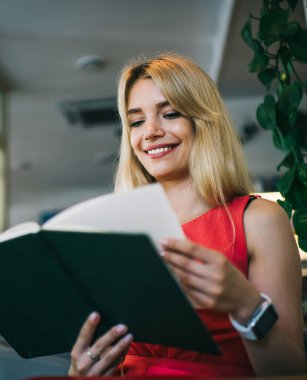 Kırmızı elbiseli mutlu genç bayandan siyah kitabın sayfalarını çeviren favori yazarının yeni romanıyla heyecanlanan kafede vakit geçiren