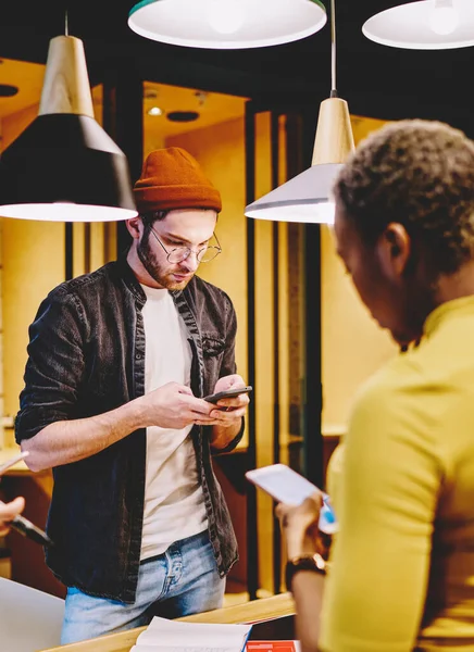 Group of hipsters ignore real communication using mobile phones for networking, crew of young multiracial millennial students checking social networks update via smartphones in coworking office