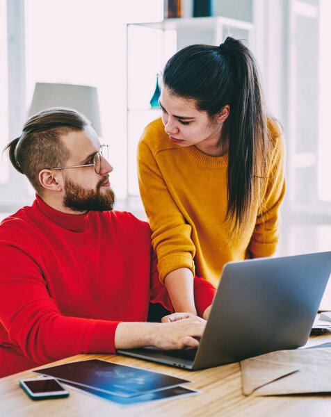 Серьезные молодые браки обсуждают покупки в интернет-магазине с помощью ноутбука в помещении дома, влюбленная пара, сотрудничающая в поиске информации в сетях, используя Wi-Fi и нетбук на рабочем столе