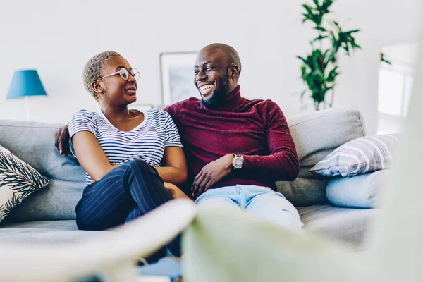 African american guy looking a his girlfriend and laughing enjoying being together at flat, happy young marriage communicating during common free time at home smiling and recalling positive moments