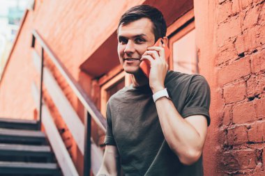 Kolunda dövmesi olan gülümseyen genç adam şehrin caddesinde yürüyen arkadaşıyla konuşmak için telefon kullanıyor.