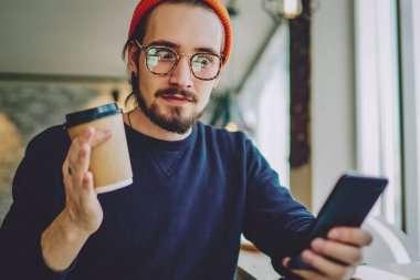 Kahve molası sırasında akıllı telefon aygıtıyla e-postaları kontrol eden şaşırmış hippi adam sosyal ağlarda sohbet ettiği için cep telefonuyla 4G 'ye bağlı şaşırmış adam.