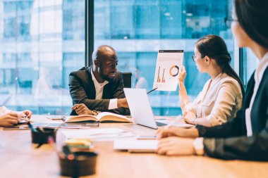 Resmi kıyafet analizi yapan çok ırklı ve zeki meslektaşlar. Pencere karşısındaki ofiste dizüstü bilgisayarlı not defterleriyle ahşap masada oturuyorlar.