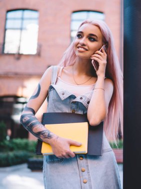 Pembe saçlı, dövmeli, gülümseyen ve yüzünü çeviren iyimser genç bir öğrenci.