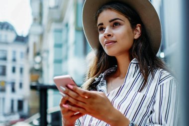 Şık şapkalı güzel bir kadın elinde cep telefonuyla blog 'da yayınlanması için makale yazmayı düşünüyor. Açık havada zaman harcayan çekici bir hippi kız akıllı telefon kullanıyor ve sohbet için 4G internet kullanıyor.