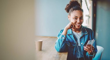 Motivasyon listesindeki favori şarkıyı cep telefonundan dinlerken şık giyinmiş, mutlu bir kadının sesli kitaptan hoşlandığı, kameraya bakan heyecanlı yeniyetme kızın portresi.