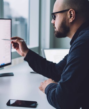 Ofisteki masadaki istatistiksel bilgilerle çalışan, gözlüklü sakallı adamın ekran görüntüsü.