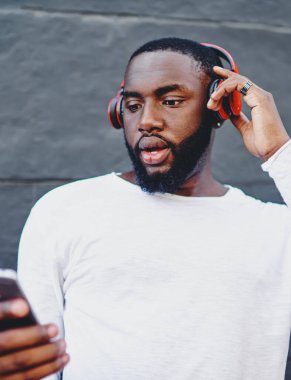 Erkek meloman içerik sitesinde yeni ses şarkıları arıyor. Uygulama fiyatından şok olmuş hissediyor. Bluetooth kulaklıkla sesli kitap dinlemek için cep telefonuyla sohbet eden adam.