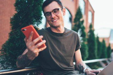 Cep telefonuyla 4G kablosuz internete bağlanan oyuncular için web sitesinde göz giysisi okuyan mutlu hippi adam cep telefonuyla web sayfalarını tarayan yetenekli, neşeli adam.