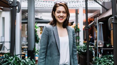 Gri ceketli, başında güneş gözlüğü olan çekici Asyalı kadın rahat kafenin yanında kameraya bakıyor ve gülümsüyor.