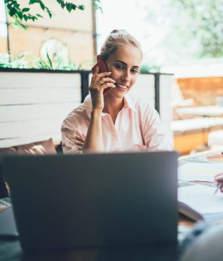 Akıllı telefondan konuşan ve bilgisayarın ekranına bakan hoş bir kadın. Meslektaşlar masada oturup dinlerken ve not defteri ve cihaz kullanarak not alırken.