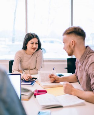 Masada otururken ve sınava hazırlanırken üniversite arkadaşına kitap ve kalemle yardım eden genç bir kadın.