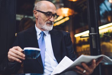 Sakallı, kahve fincanı bardaklı ve takım elbiseli, camlara gazete okuyan yakışıklı adam.