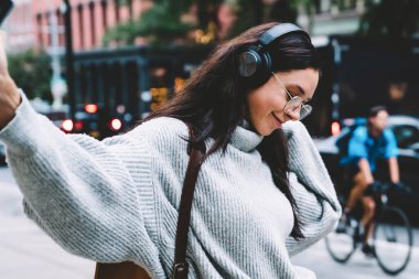 New York caddesinde kulaklıkla müzik dinlerken sokakta yürüyüp dans eden süveter ve gözlüklü neşeli bir kadın.