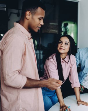 Ofis masasının yanındaki iş birliği sırasında proje fikirleri hakkında iletişim kuran gündelik gömlekli profesyonel hippi erkekler, çok kültürlü erkek ve kadın meslektaşlar detay ve bilgiyi tartışıyor.