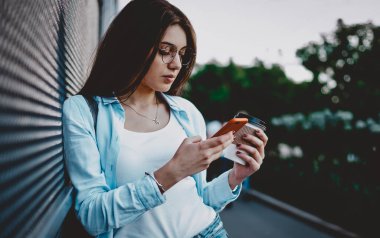 Sokak ortasında 4G internet bağlantısı kullanarak sosyal ağlarda sohbet etmek için kahve ile şık giyimli hippi kız. Şehir ortamında cep telefonu profilini güncelleyen genç bir kadın.