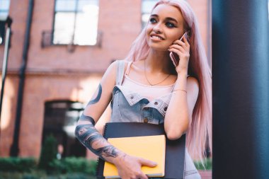 Pembe saçlı, dövmeli, gülümseyen ve yüzünü çeviren iyimser genç bir öğrenci.