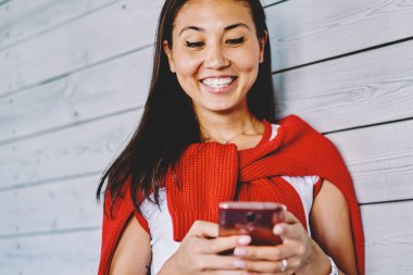 Neşeli Çinli genç bir kadın cep telefonuyla internetten mesajlaşarak ücretsiz 4G interneti kullanıyor. Cep telefonundan video izlerken gülen pozitif Japon hipster kız.