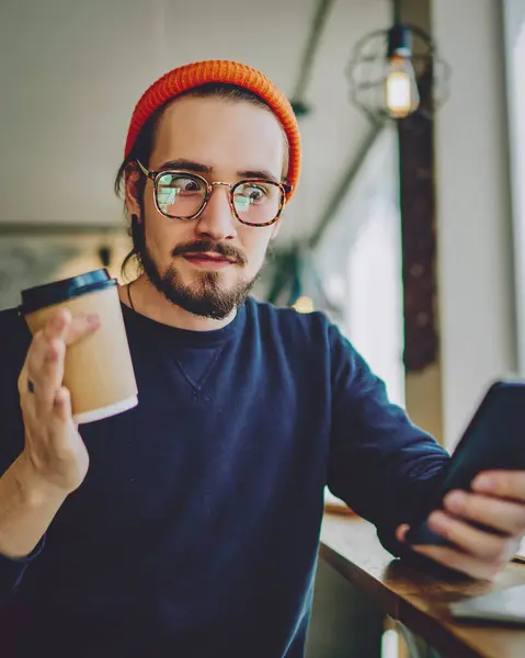 Amazed hipster guy with shocked expression on face checking mails via smartphone device during coffee break, surprised man connected to 4g wireless on cellphone for chatting in social networks