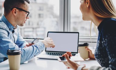 İki erkek ve kadın serbest çalışan ellerinde akıllı telefonla modern dizüstü bilgisayarda internet içeriğiniz için boş ekran alanı olan iş web sitelerini izliyorlar.