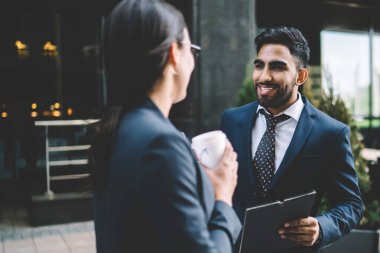 Keyifli iş arkadaşları ellerinde bir fincan kahve ve klasörle resmi siyah takım elbiseli ofiste birbirleriyle sohbet ediyorlar.