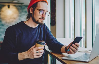 Gözlüklü ciddi bir erkek blogcu, internet sitesi içeriğini ararken akıllı telefon uygulaması üzerinden çevrimiçi video izleyerek göz koruması sağlıyor. Kafkasyalı hippi, kahve molasında haber okuyor.