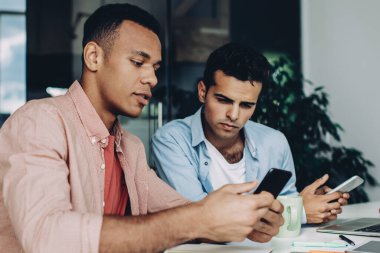 Çeşitli erkek çalışanlar iş konferansı için internet üzerinden mobil cihazlar üzerinde internete baktıkları için 4G 'ye bağlı online bilet alıyorlar, çok ırklı iş arkadaşları şirketin internet sitesinden bilgi tartışıyorlar.