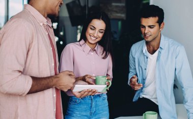 Neşeli çeşitli erkek ve kadınlar ofis içi iş günlerinde modern dokunmatik ped üzerinden komik web videoları izliyorlar, olumlu genç çalışanlar online iletişim için teknolojiyi kullanıyorlar.