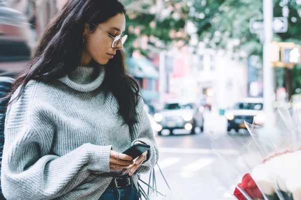 Gri kazaklı ve gözlüklü bir kadın elinde alışveriş torbalarıyla kaldırımda duruyor ve New York 'ta sokakta telefonla dikiliyor.