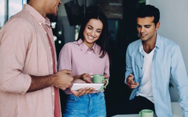 Neşeli çeşitli erkek ve kadınlar ofis içi iş günlerinde modern dokunmatik ped üzerinden komik web videoları izliyorlar, olumlu genç çalışanlar online iletişim için teknolojiyi kullanıyorlar.