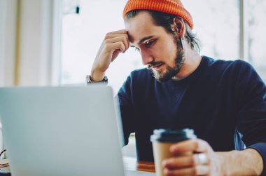 Kafkas erkek öğrenci yorgun hissediyor web sayfasında internete bağlı dizüstü bilgisayarla sıkıcı eğitim webinar izlerken, yetenekli serbest yazar web sitesinde yararlı makaleler okuyor