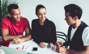 Genç, çok ırklı erkek ve kadın meslektaşların, proje stratejisi planlarken fikir alışverişinde bulunması ve fikir alışverişinde bulunması, kapalı alanlarda iş birliği yapan başarılı bir grup genç.
