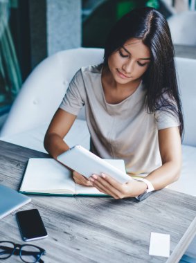 Araştırmalar için taşınabilir bilgisayar kullanan konsantre esmer kadın, blogda yayınlanması için yetenekli kadın serbest yazar, kafede uzaktan çalışma yapıyor.