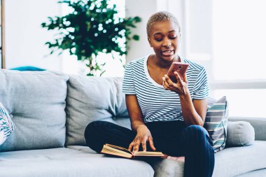 Genç Afrikalı Amerikalı bir kadın, arkadaşı için sesli mesaj bırakıyor. Oturma odasındaki koltukta cep telefonu uygulaması kullanıyor. Koyu tenli hippi kız, akıllı telefonuyla konuşarak bilgi topluyor.