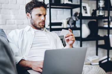 Düşünceli Kafkasyalı adam bilgisayarla ve kablosuz internetle alışveriş yapmak için evden bilgi toplamaya odaklanmış. Ciddi hippi adam kredi kartı numarasıyla Netbook 'ta işlem yapıyor.